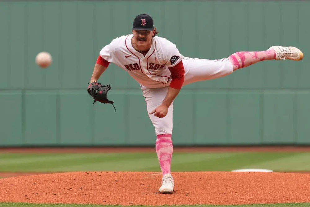 Payton Tolle throws a pitch at Fenway Park with his left leg extended and a green wall in the background.